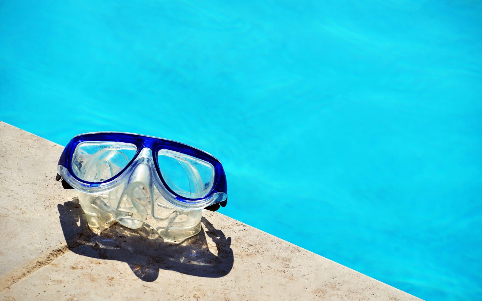 Snorkel mask resting on the sun-warmed pool edge beside the bright blue water